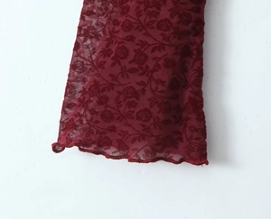 Close-up of burgundy lace sleeve with rose pattern and flared ruffle cuffs detail