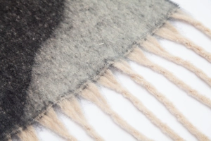 Dettaglio di sciarpa spessa grigia in mohair con trama morbida e nappe beige