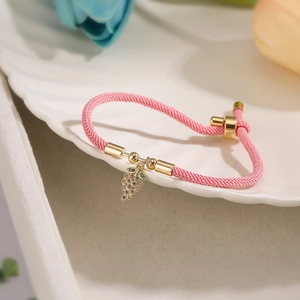 Macro detail of pink braided drawstring bracelet with a gold grape crystal charm