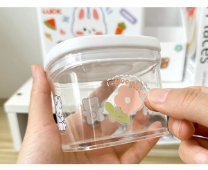 Detail of hand holding a clear storage jar with cute cartoon stickers for kids DIY