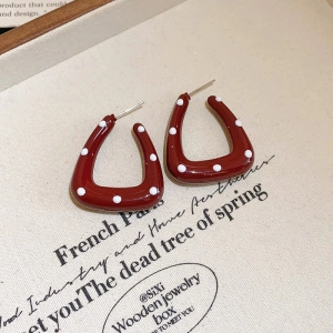 Macro detail of red enamel U-shaped earrings with white polka dots on aesthetic background