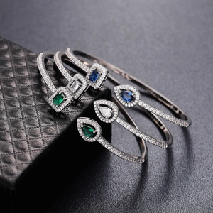 Detail of open brass bracelets with green, blue, and white zircon stones on jewelry box