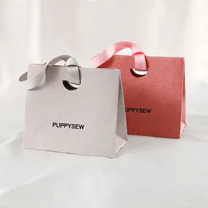 Minimalist paper gift bags with circular handles and satin ribbons in pink and grey