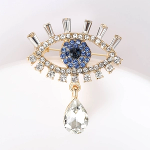Detailed close-up of gold eye brooch with blue crystals and elegant teardrop pendant