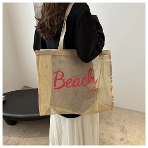 Detail view of khaki mesh tote bag with Beach Vibes text carried by a person