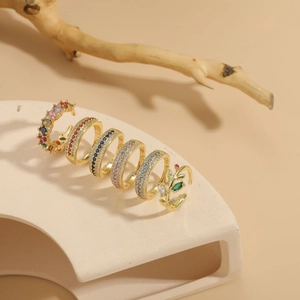 Set of six gold-plated zircon rings featuring colorful gems and leaf designs on sandy base