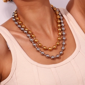 Détail d'un collier à billes superposé en or et argent au cou au style industriel épuré