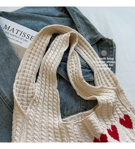 Detalle de bolso tote de punto crema con diseño de corazón rojo sobre tela vaquera