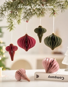 Detail of Christmas paper honeycomb ball ornaments hanging on green pine branches with a warm glow