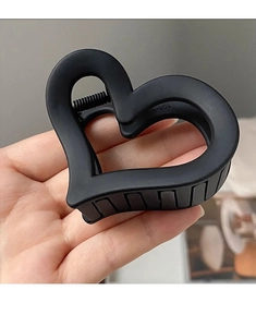 Detail showing hand holding a matte black heart-shaped hair claw clip accessory