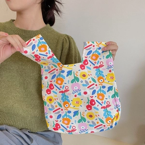 Floral canvas wrist bag shown held by a model wearing a green sweater on neutral backdrop