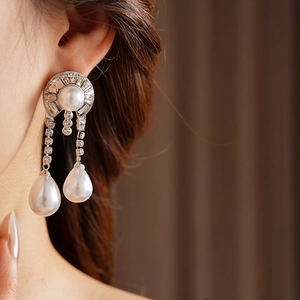 Macro view of crystal encrusted drop pearl earrings worn by a model on soft background