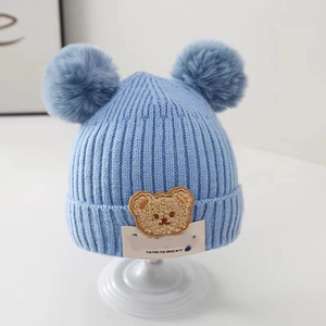 Detail of blue knitted baby hat featuring double pom-poms and a cute brown bear patch