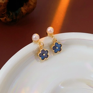 Detail of blue flower earrings with white pearls and gold plating on a ceramic dish