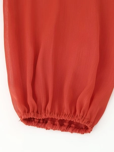 Detail of orange chiffon long sleeve dress showing elastic cuff texture and fabric quality