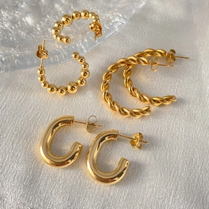 Detailed macro shot of three pairs of golden stainless steel earrings on silk background.