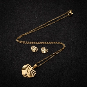 Golden heart-shaped swirl necklace and earrings set on a black textured background