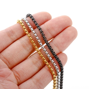 Detail of square box chains in gold, silver, and black stainless steel held by hand
