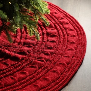 Red cable knit Christmas tree skirt with thick wool texture on dark wood floor