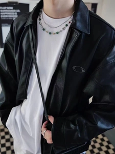 Detail of a black PU leather jacket with a metal zipper and layered beaded necklace