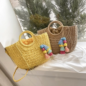 Detail of woven straw tote bag with ring handle and colorful pom-pom tassel charm