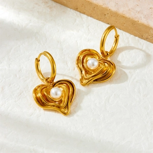 Gold-plated heart earrings with round pearl inlay on a textured stone background