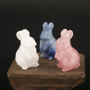 Three hand-carved natural crystal rabbit figurines in pink blue and white on wooden base