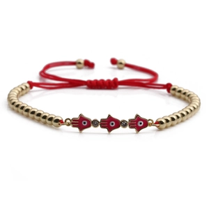 Detail of red braided string bracelet with golden Hamsa Hand charms and zircon accents