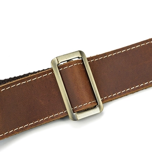 Detail of vintage brown leather strap with white stitching and bronze metal buckle