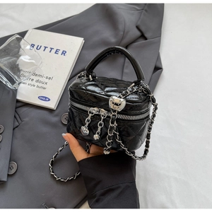 Detail of a black quilted box bag featuring silver heart charm and metal chain strap