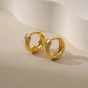 Close-up of polished 18K gold plated thick hoop earrings on a minimalist background