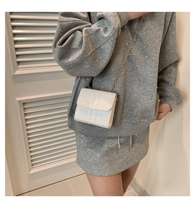 Close-up of white quilted mini square bag with golden chain strap on model