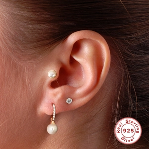 Close-up of 925 sterling silver heart and pearl cartilage piercings on a female ear