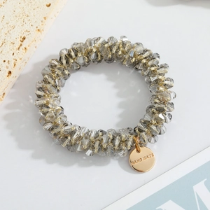 Close-up of handmade elastic hair tie with gray crystal beads and golden engraved tag