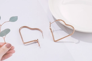 Détail de grandes boucles d'oreilles cœur en or rose avec texture martelée sur plateau
