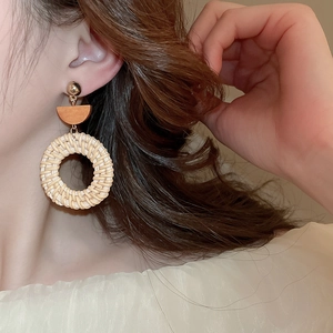 Detail of bohemian round straw woven earrings with wooden accent on model