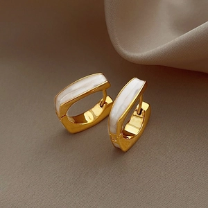 Detail of gold rectangular earrings with white shell inlay on soft silk background