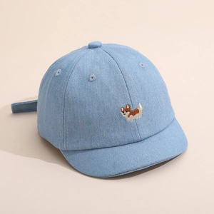 Détail de la casquette bébé en denim avec broderie de chien corgi sur tissu bleu clair