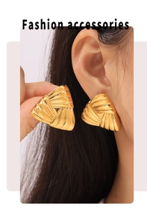 Macro detail of gold-plated geometric triangle earrings with ribbed texture on ear