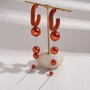 Detailed view of oversized acrylic pearl tassel earrings on a gold stand base
