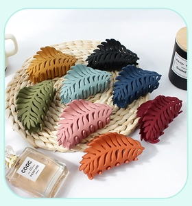 Flat lay of eight colorful leaf-shaped matte hair claws on a woven mat for bun styling