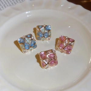 Detail of square gold plated stud earrings with blue and pink enamel on a porcelain plate