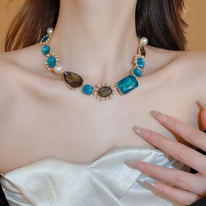 Close-up of model wearing a vintage gold necklace with blue and amber faceted gems and pearls