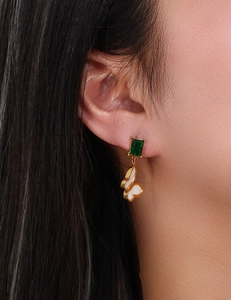 Close-up of a gold butterfly earring with a green square zircon on a female model