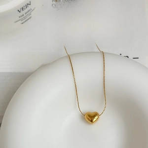 Detailed close-up of a polished gold heart pendant necklace on minimalist background