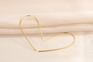 Dettaglio di orecchini a cerchio dorati a forma di U su tessuto beige strutturato