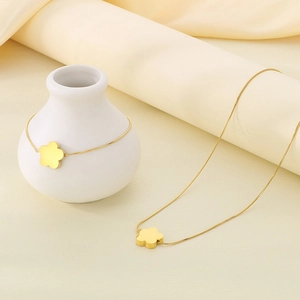 Detail view of gold clover pendant necklace and snake chain bracelet set on beige background