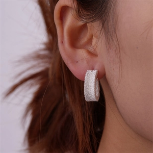 Macro side view of silver matte geometric C-shaped hoop earrings on a female model
