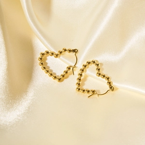 Dettaglio ravvicinato di orecchini a cuore con perline dorate su seta beige elegante