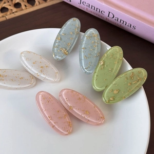 Set of eight colorful oval resin hair clips with gold foil flakes on a white plate